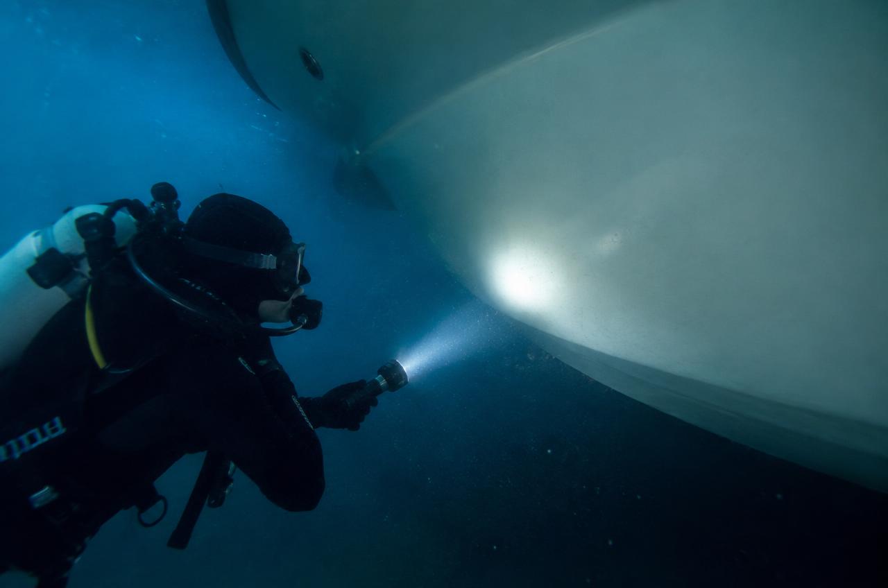 Diver inspecting a yacht hull with an underwater light
